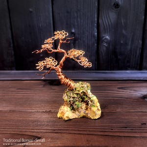 May include: A small copper wire bonsai tree sculpture with a green moss base. The tree is on a wooden surface.