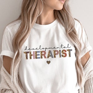 May include: White t-shirt with the text "developmental THERAPIST" in leopard print and pink and gray lettering. A small heart is below the text.