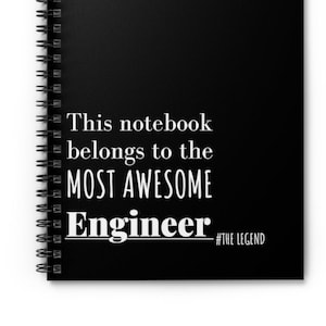 May include: Black spiral-bound notebook with white text that reads "This notebook belongs to the MOST AWESOME Engineer #THE LEGEND". The notebook is a standard size and has a black cover.