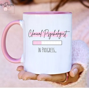 May include: White ceramic mug with a pink rim and handle. The mug has a pink and white progress bar with the text "Clinical Psychologist" and "IN PROGRESS..." printed on it.