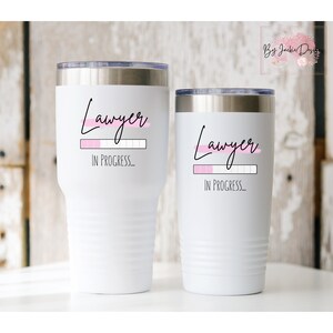 K&ouml;nnte beinhalten: Zwei wei&szlig;e Becher mit einem schwarzen und rosafarbenen Design, auf dem "Anwalt in Arbeit..." steht.