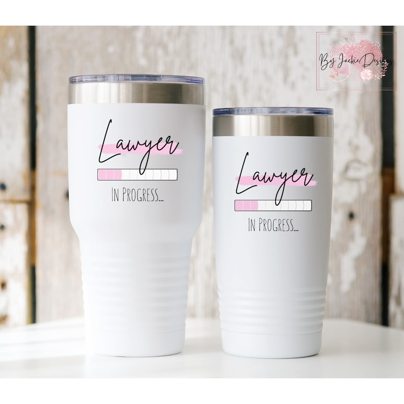 K&ouml;nnte beinhalten: Zwei wei&szlig;e Becher mit einem schwarzen und rosafarbenen Design, auf dem "Anwalt in Arbeit..." steht.
