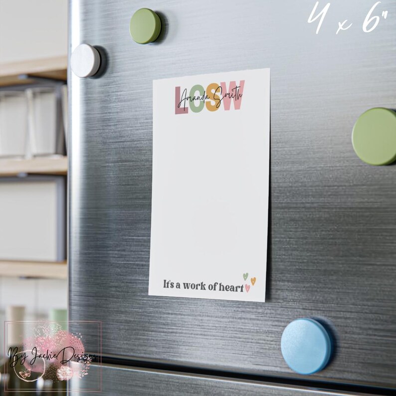 May include: A white notepad with the text "LOOSW Amanda Smith" in colorful letters is attached to a refrigerator with magnets. The notepad has the phrase "It's a work of heart" at the bottom, with small heart graphics. The notepad measures 4 x 6 inches.