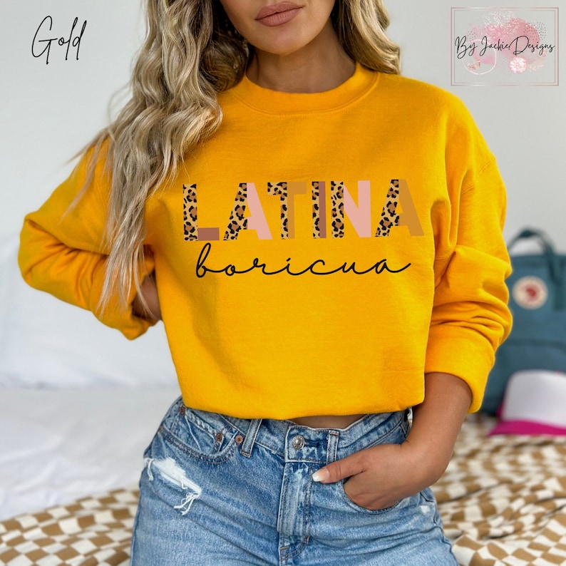 Puede incluir: Una sudadera amarilla con las palabras "LATINA boricua" impresas en la parte delantera. Las letras est&aacute;n en un patr&oacute;n de estampado de leopardo con acentos rosados.