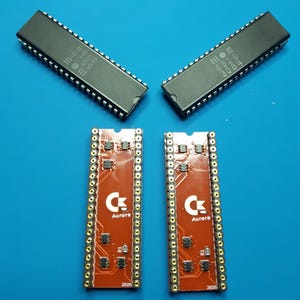 May include: Two black integrated circuit chips with silver pins and printed numbers, paired with two rectangular red circuit boards featuring gold-plated pin headers, the Aurora logo, and the year 2020 printed in white on the surface.