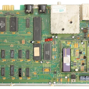 Può includere: Una scheda a circuito stampato verde con vari componenti elettronici, tra cui chip, resistori e condensatori. La scheda ha un'etichetta che recita "USI 94V-0".