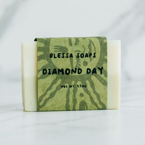 May include: A bar of white soap with a green label that reads "Blesa Soaps Diamond Day Net Wt. 4.5 oz"