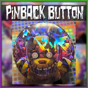 May include: A pinback button with a holographic design featuring a cartoon character with a menacing grin. The button has the text "PINBACK BUTTON" in a white, distressed font. The background has a rainbow effect.