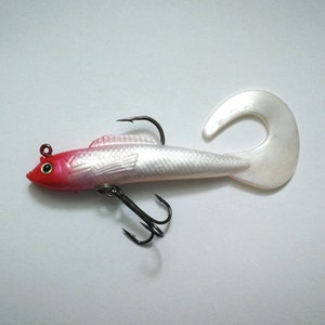 May include: A fishing lure shaped like a fish, with a red head, silver body, and a white, curved tail. It has two black hooks and a small red eye. The lure is designed to attract fish.