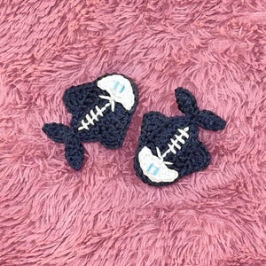 May include: Two crocheted black fish with white skeleton details on a pink fuzzy surface.