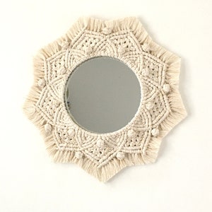 Peut inclure: Un miroir en macramé blanc avec un miroir circulaire au centre. Le miroir est entouré d'un motif en macramé en forme d'étoile avec des franges.