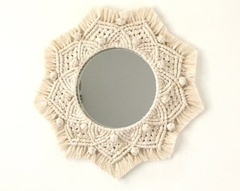 Peut inclure: Un miroir en macramé blanc avec un miroir circulaire au centre. Le miroir est entouré d'un motif en macramé en forme d'étoile avec des franges.