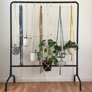 Peut inclure: Un support à plantes en métal noir avec huit suspensions macramées, chacune tenant une plante en pot. Les suspensions sont faites de fils de différentes couleurs, dont le blanc, le bleu, le vert et le jaune.