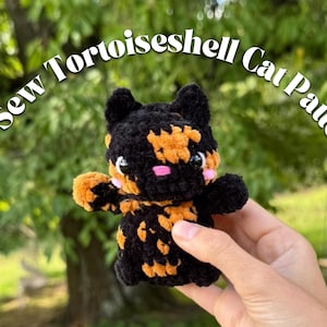 Könnte beinhalten: Handgefertigtes Schildpatt-Katzenplüschtier in Schwarz und Orange mit rosa Akzenten. Der Text "No-Sew Tortoiseshell Cat Pattern" ist über der Katze angeordnet. Verschwommener grüner Hintergrund.