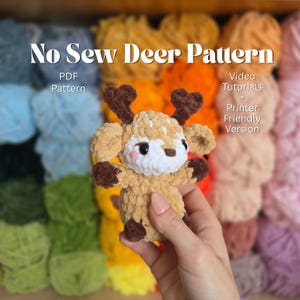 May include: A crocheted deer plushie with brown antlers, hooves, and spots, and a white face with pink cheeks. The text "No Sew Deer Pattern" is at the top, with "PDF Pattern" below it. The text "Video Tutorials + Printer Friendly Version" is on the right.