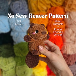 May include: A brown crocheted beaver plush toy with a dark brown tail and accents. The beaver has a pink nose and black eyes. The text "No Sew Beaver Pattern" is at the top of the image, with additional text below.
