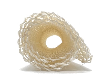 Può includere: Un primo piano di una spugna di luffa bianca arrotolata. La luffa è fatta di fibre naturali e ha una consistenza ruvida.