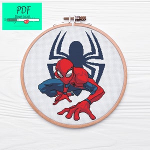 May include: A cross-stitch pattern of Spider-Man in a red and blue suit, crouching with his arms outstretched. The background is a white fabric with a black spider web design.