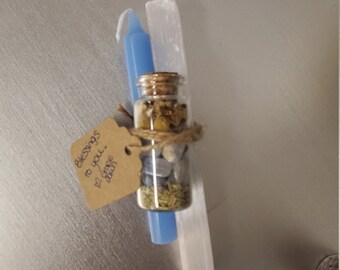 May include: A small glass bottle filled with crystals, herbs, and a tag that reads "Blessings to you. Grace & Joy". The bottle is tied with twine and is next to a blue candle and a white crystal.