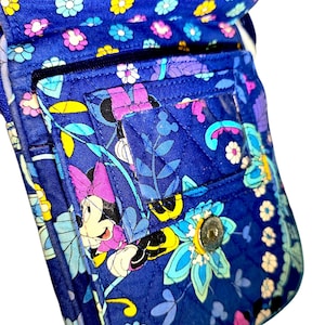 May include: A quilted fabric crossbody bag in a vibrant blue featuring a repeating pattern of colorful flowers and Minnie Mouse characters. The bag includes a front flap with a clear plastic ID window, a metal snap closure, and a zippered pocket.