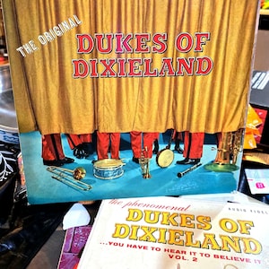 May include: Vintage vinyl record album cover for "Dukes of Dixieland" featuring a yellow curtain and musicians in red pants. The album cover has the text "CURTAIN GOING UP" and "THE ORIGINAL". The album is labeled "ROULETTE" and "DYNAMIC HIGH FIDELITY".