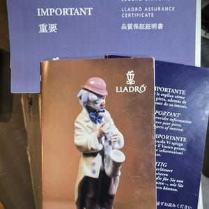 May include: A porcelain figurine of a clown from the Circus Collection, holding a saxophone. The clown wears a white coat, black pants, and a pink hat. Accompanying documents are visible, including a certificate and a brochure.