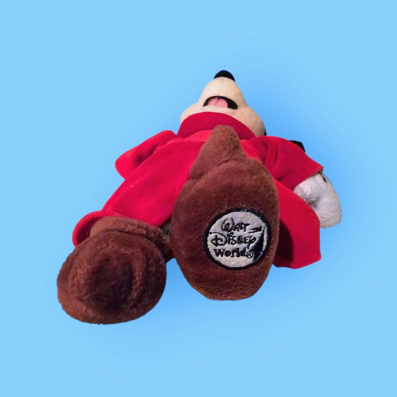 May include: Red plush Mickey Mouse wearing a red robe with a brown face and brown feet. The robe has a "Walt Disney World" logo on the back.