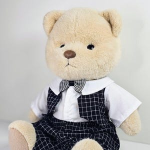 May include: A plush teddy bear wearing a white shirt, a black and white checkered vest, and black and white checkered pants with a black and white bow tie.