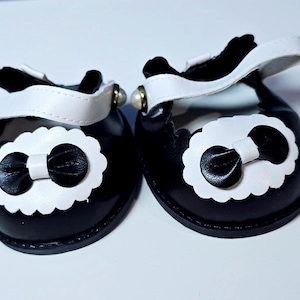May include: A pair of black and white doll shoes with a white bow on each shoe.