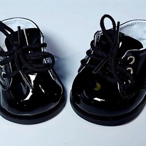 May include: A pair of black patent leather shoes with black laces. The shoes have a rounded toe and a low heel.