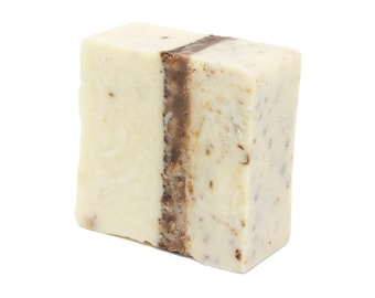 Può includere: Una saponetta artigianale con uno strato marrone al centro. Il sapone è bianco e ha un aspetto maculato.