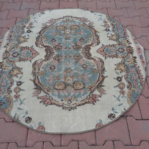 May include: A round, cream-colored rug with a floral pattern in shades of brown, pink, and blue. The rug has a fringed edge.