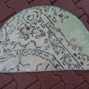 May include: A light green and cream coloured half-round rug with a floral pattern. The rug has a fringe border.