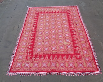 Könnte beinhalten: Ein rechteckiges rotes Textil mit einem komplizierten gold-weißen Stickmuster aus sich wiederholenden floralen und geometrischen Motiven. Der Stoff ist an allen vier Kanten des rechteckigen Stücks mit einer dekorativen weißen Bogenkante versehen.