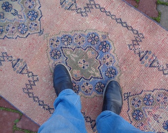 May include: A pair of blue jeans with black shoes standing on a pink and blue patterned rug.