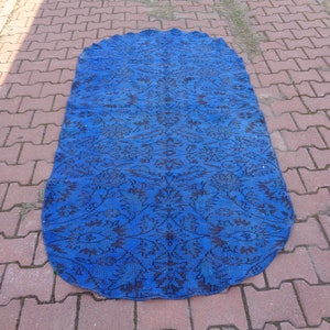 May include: A blue and black oval rug with a floral pattern. The rug is made of a woven material and has a fringed edge.