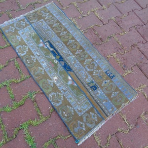 May include: A vintage Turkish runner rug with a blue, green, and brown geometric pattern. The rug has a fringe border and is lying on a brick surface.
