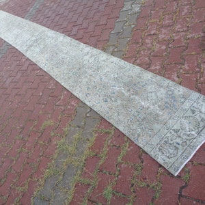 May include: A long, white and blue patterned rug with a floral design. The rug is rolled up and lying on a red brick surface.