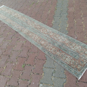 May include: A long, rectangular rug with an intricate floral pattern in shades of red, beige, and green. The rug has a distressed, vintage appearance and is placed on a brick surface. The rug's dimensions are not visible.