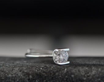 May include: A silver ring with a single clear round gemstone set in a prong setting.