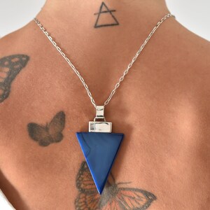 May include: A silver chain necklace with a triangular pendant made of dark blue lapis lazuli. The pendant is set in a silver frame.