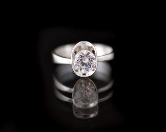 May include: A silver ring with a large, clear, round gemstone set in a bezel setting.