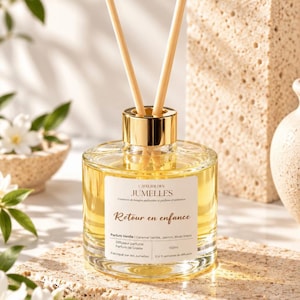 Peut inclure: Un diffuseur de parfum à bâtonnets en verre transparent contenant un liquide doré, avec un col doré et des tiges en bois clair. L'étiquette blanche porte le texte L'ATELIER DES JUMELLES, Retour en enfance, Parfum Vanille, 150ml.
