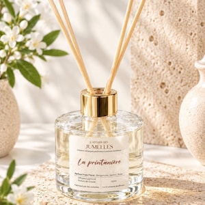 Peut inclure: Un flacon diffuseur à roseaux en verre transparent avec un bouchon doré et plusieurs tiges en bois. L'étiquette indique L'ATELIER DES JUMELLES, La printanière, Parfum Frais Floral, Bergamote, Jasmin, Rose, Diffuseur parfumé, 150ml, Fabriqué par les Jumelles.