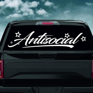 Puede incluir: Calcomanía de vinilo blanco con la palabra "Antisocial" en cursiva, adornada con estrellas. La calcomanía se muestra en la ventana trasera negra de un vehículo, con un cielo nublado de fondo.