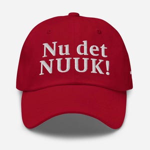 Può includere: Cappellino da baseball rosso con la scritta ricamata "Nu det NUUK!" in bianco. Il cappellino ha una visiera curva e un design a sei pannelli, adatto per l'uso quotidiano.