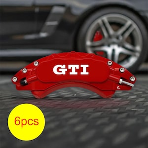 Könnte beinhalten: Ein leuchtend roter GTI-Bremssattel mit weißer Schrift, vor einem verschwommenen Autorad. Ein gelber Kreis mit "6pcs" befindet sich unten links. Dies ist ein Autoteil.