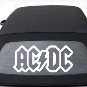 Puede incluir: Adhesivo blanco con el logotipo de AC/DC aplicado en la ventana trasera de un coche descapotable negro. El logotipo muestra el nombre de la banda en una fuente estilizada con un rayo.