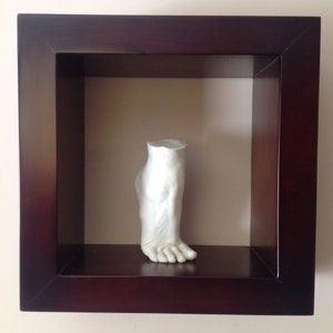 May include: A white plaster cast of a foot, displayed in a dark wood frame.