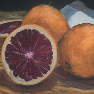 K&ouml;nnte beinhalten: Ein Stillleben mit drei Orangen, von denen zwei halbiert sind und ihr tiefrotes Fruchtfleisch zeigen. Die Orangen sind auf einem Holztisch mit einem blau-wei&szlig;en Tuch im Hintergrund angeordnet.